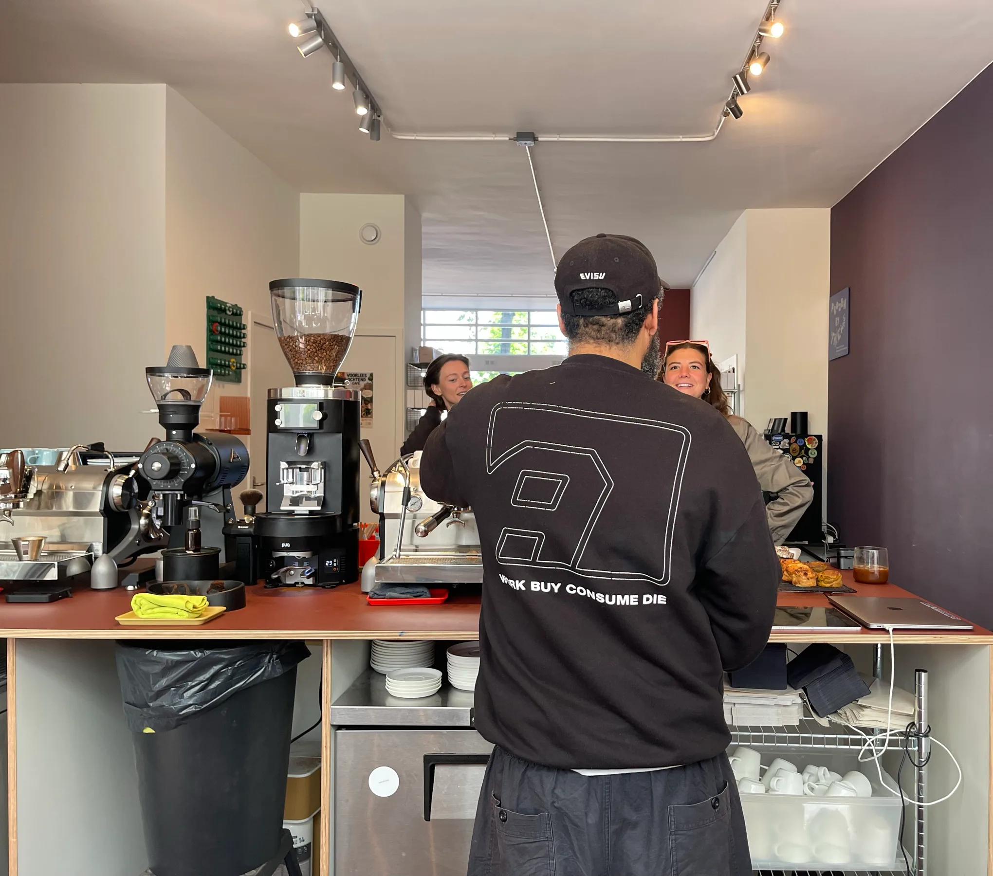 A barista chatting with two regulars across the counter at Akhi 'n Friends